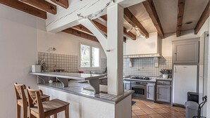 Een keuken met een centraal eiland, houten stoelen en een betegelde achterwand.