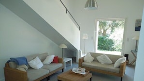 Un salon avec deux canapés, une table basse et un fauteuil en osier. Un escalier mène à un niveau supérieur.