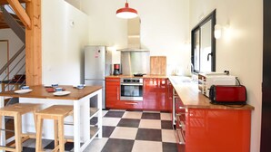 Een compacte keuken met een zwart-witte vloer, houten krukken, een rode hanglamp en moderne apparaten.