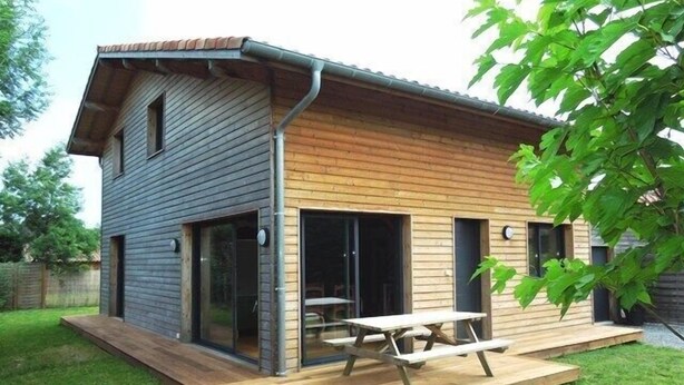 Een modern huis met een houten terras en een picknicktafel.
