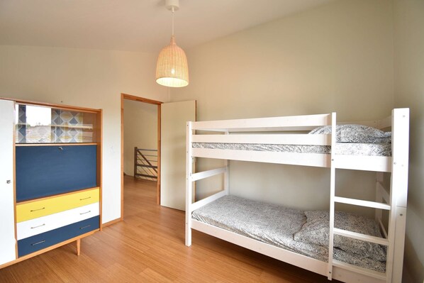 Una habitación con literas, un armario con cajones y una lámpara colgante.