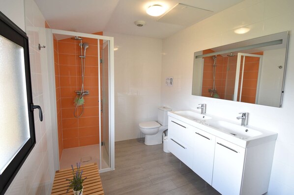 Een moderne badkamer met een douche, toilet en een wastafel met dubbele wastafel.