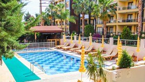 A pool area with checkered tiles, lounge chairs, and umbrellas. - Yaman Life Hotel (Alanya)