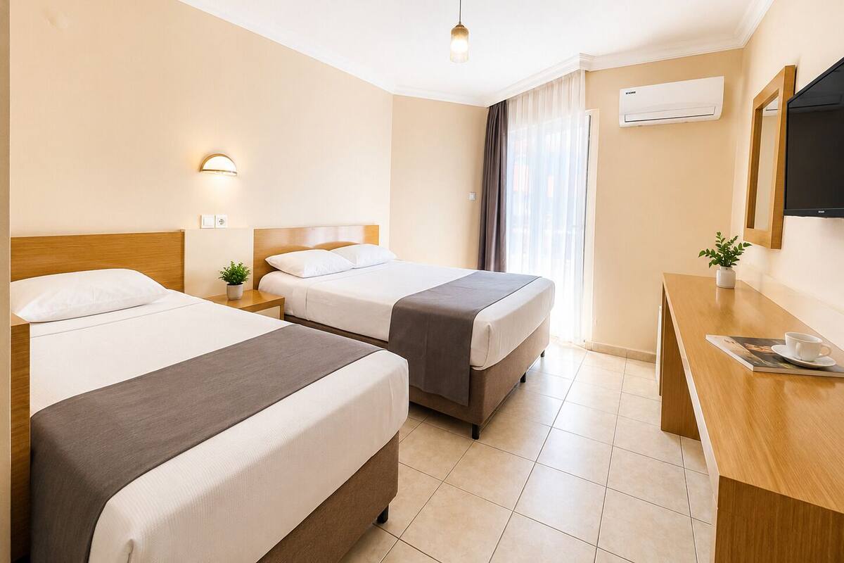 A hotel room with two beds, a desk, a TV, and a window with curtains.