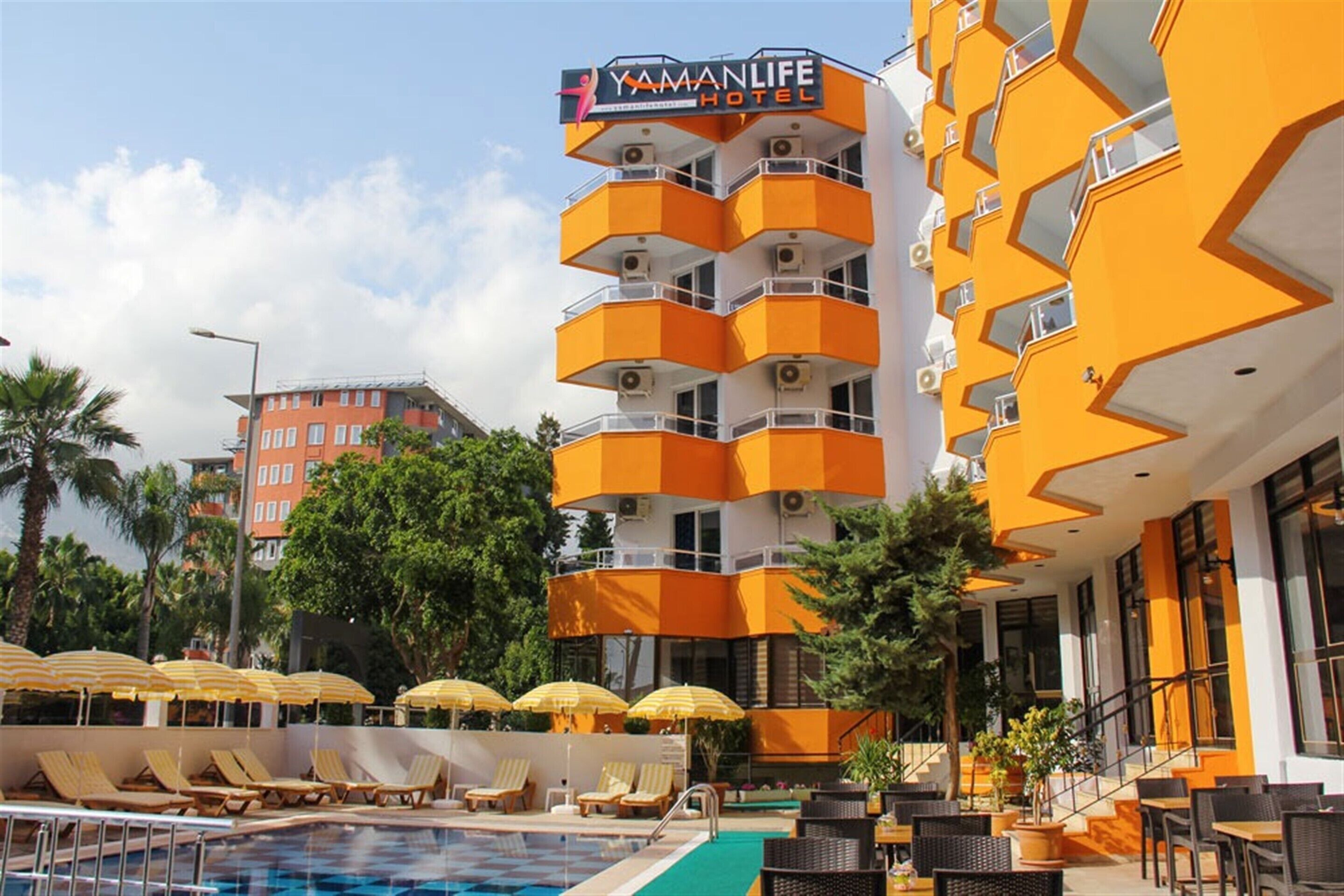 A Yamanlife Hotel with a pool area, outdoor seating, and a distinctive orange and white building facade.