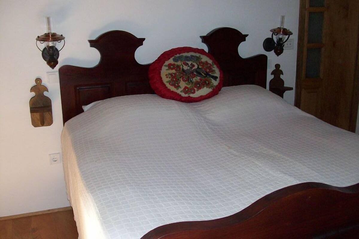A bed with a wooden headboard, a quilted white bedspread, and a decorative pillow with a floral design.