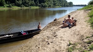 A sandy beach with a calm river, a small boat docked at the shore, and people relaxing by the water. - Ethno Village Stara Lonja (Sisak)
