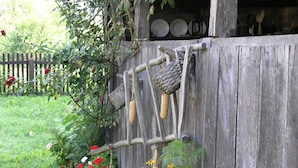 A rustic wooden structure with a wooden fence, a corn cob hanging from a wooden beam, and a variety of flowers in the foreground. - Ethno Village Stara Lonja (Sisak)