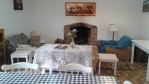 Un salón acogedor con chimenea, una mesa de comedor con mantel a cuadros y un sofá con una manta azul.