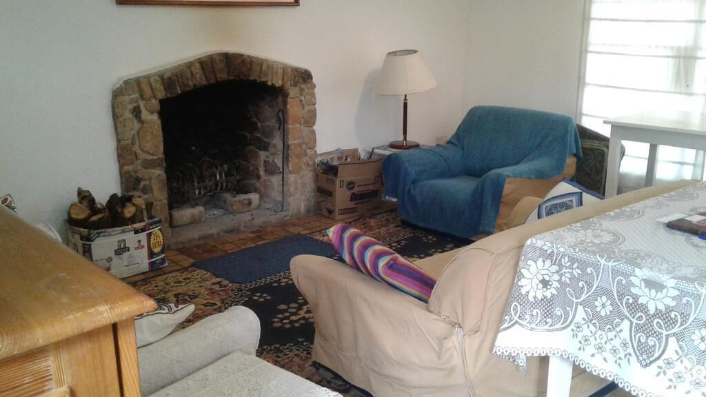 A cozy living room with a stone fireplace, a blue armchair, a beige sofa, and a patterned rug.