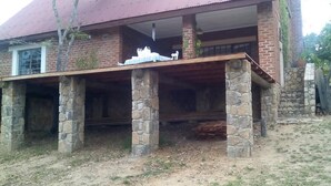 Un edificio rústico con un porche cubierto sostenido por pilares de piedra, fachada de ladrillo y techo rojo.