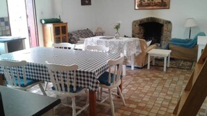 A dining area with a checkered tablecloth, white chairs, a small round table with a lace tablecloth, a fireplace, and a sofa with a blue blanket. - Paz Cottage (Juliasdale)