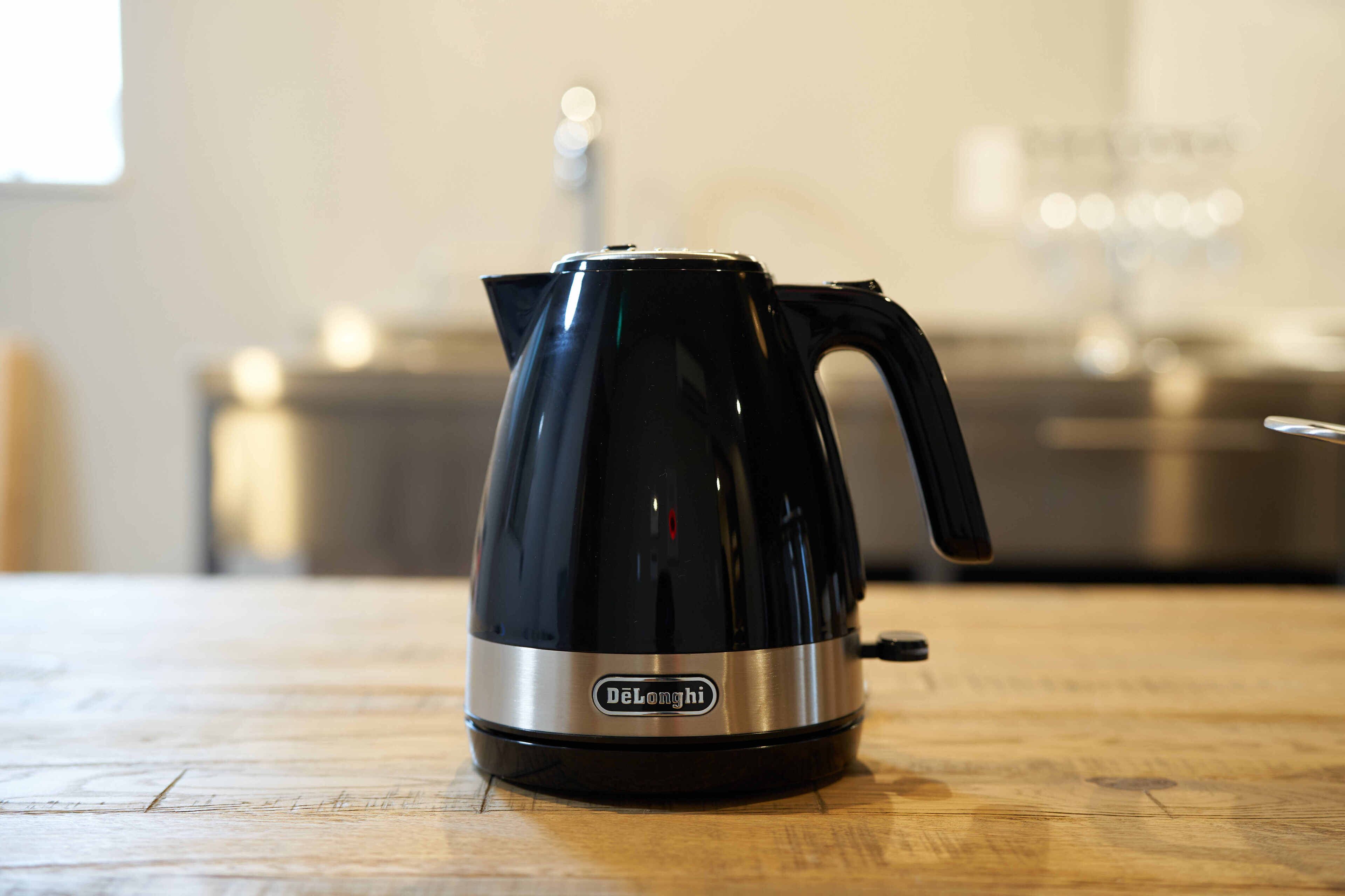A black DeLonghi electric kettle on a wooden table.