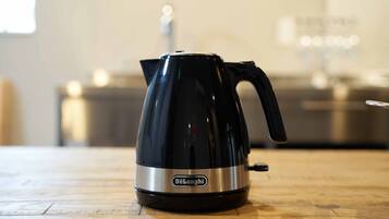 A black DeLonghi electric kettle on a wooden table.