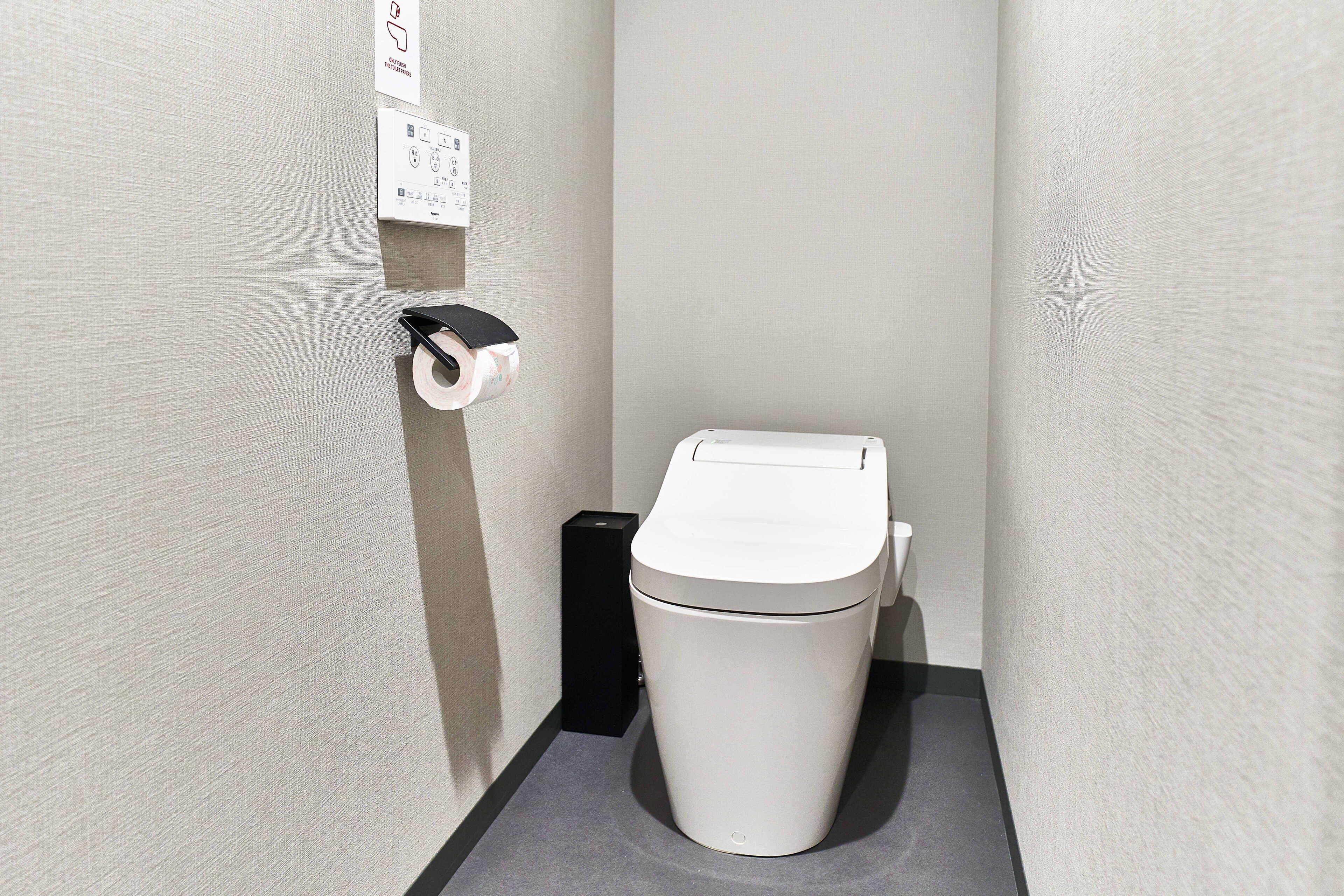 A small, modern bathroom with a toilet, a paper towel dispenser, and a trash bin.