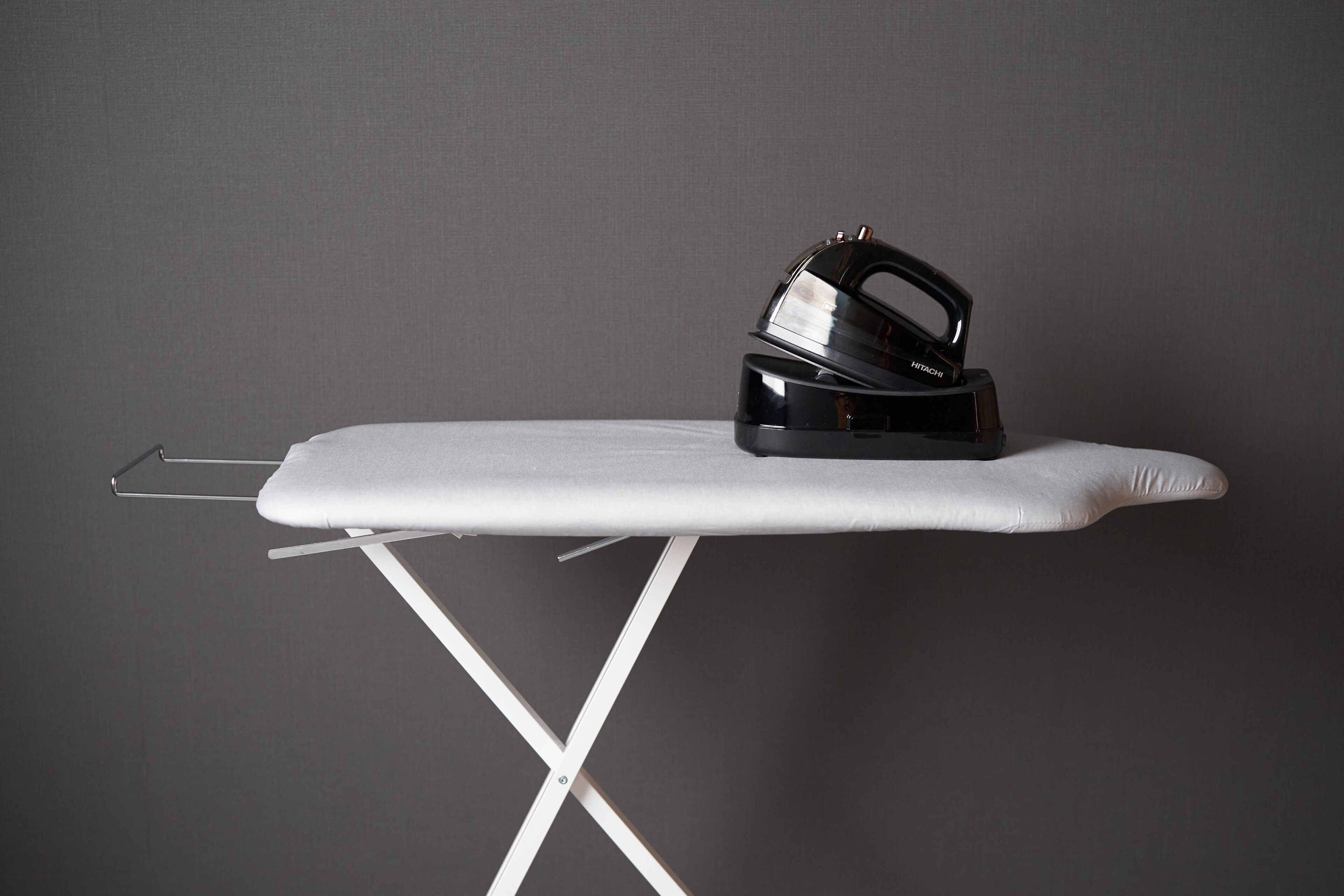 A white ironing board with a black iron placed on it, set against a plain wall.