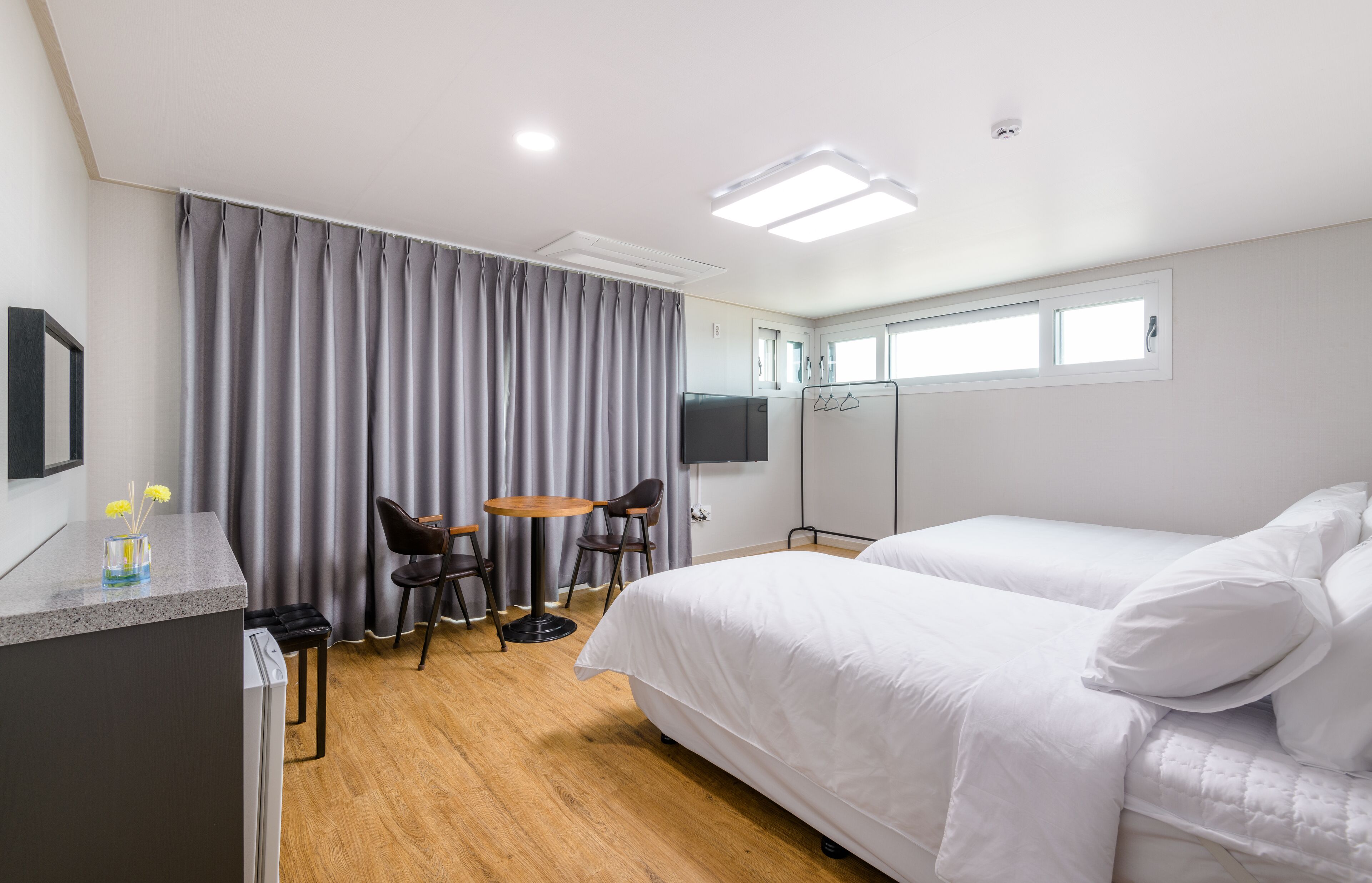 Habitación de hotel con cama, escritorio con silla, una pequeña mesa con dos sillas, televisor y ventana.