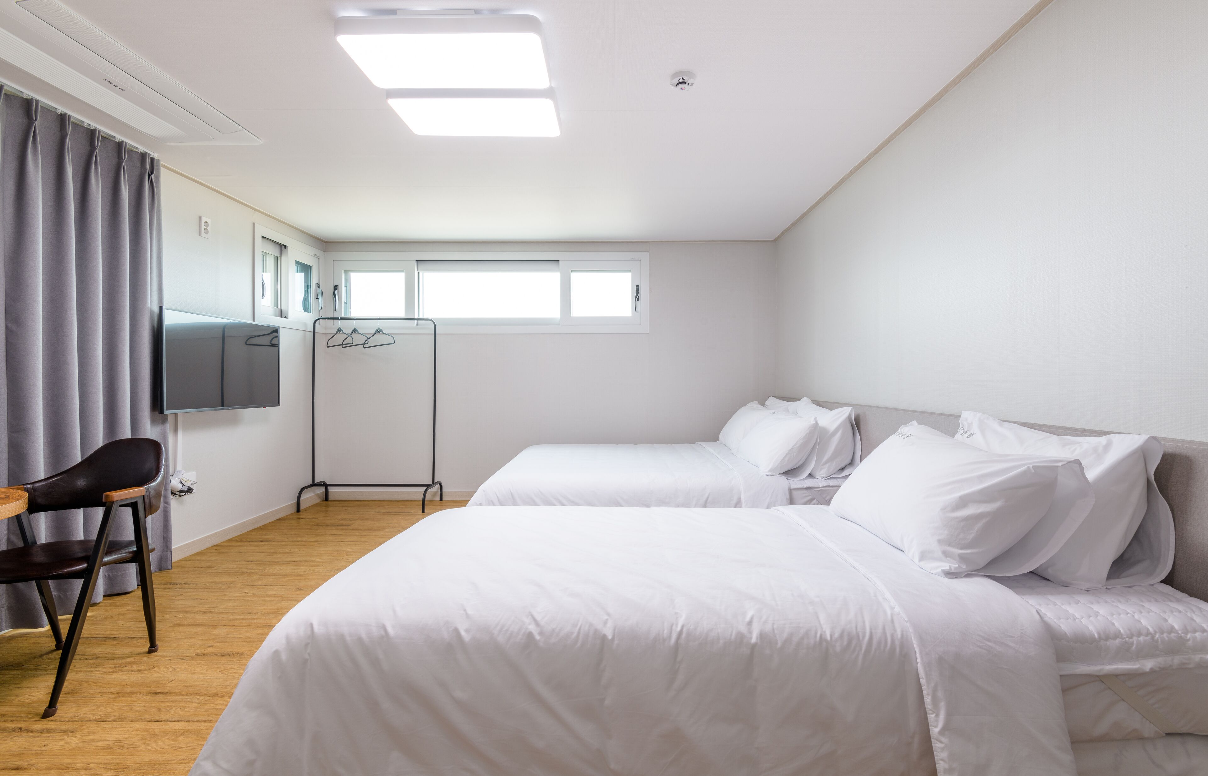 A hotel room with two beds, a desk, a chair, a flat-screen TV, and a window with curtains.