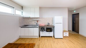 A compact kitchen with white cabinets, a microwave, a kettle, and a refrigerator. - Swimeong Nolmeong Guesthouse&Pension (Jeju City)