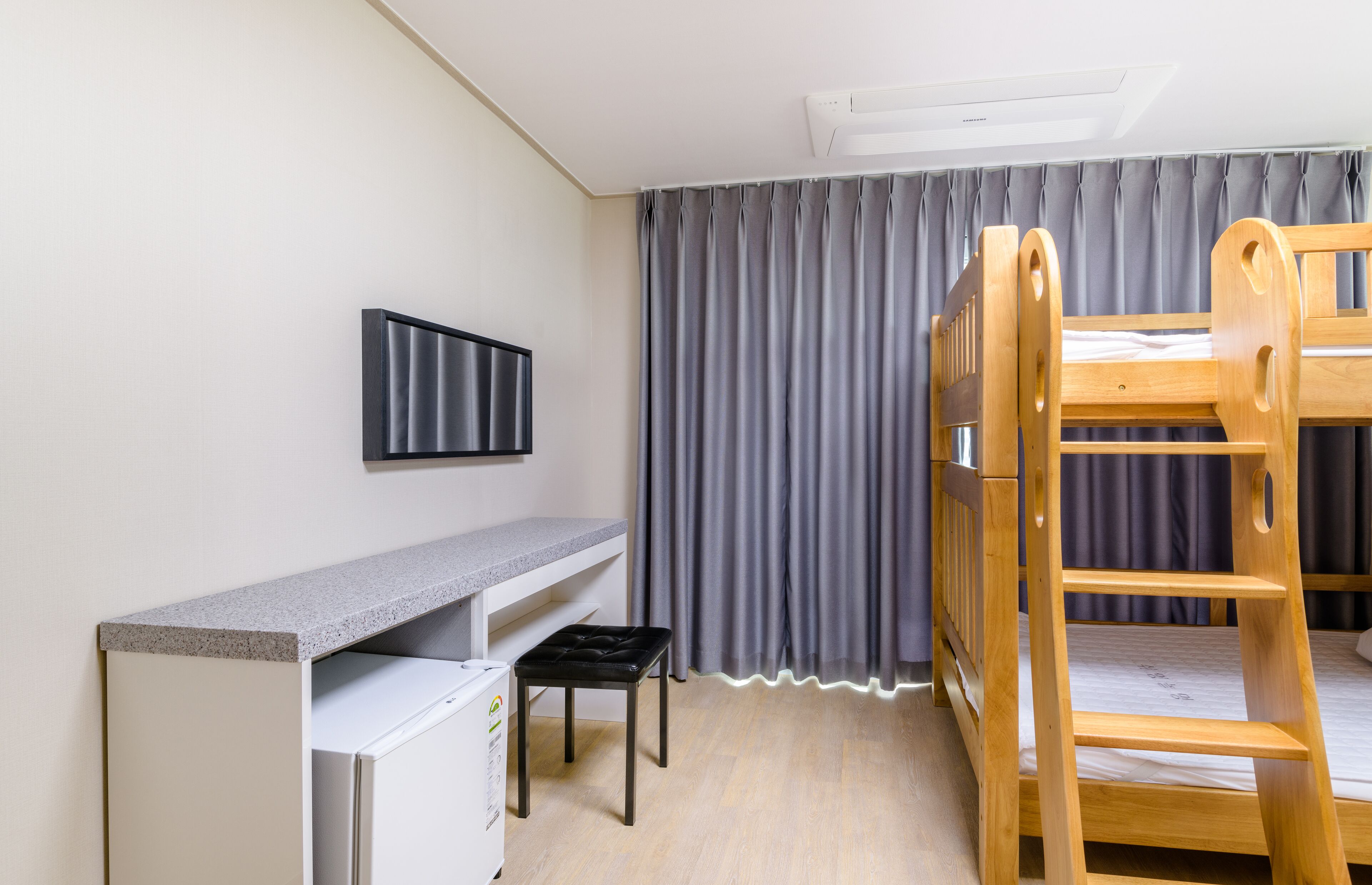 A child's bunk bed with a desk and chair, a television, and a grey curtain.