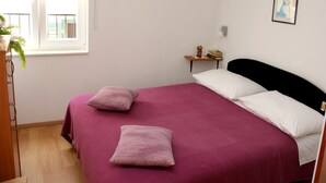 Camera da letto con un letto, due cuscini, un comodino, una finestra e un quadro appeso al muro.