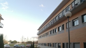 A multi-story building with a brick facade, a balcony on the upper floor, and a parking area with several cars. - Residencia La Ribera (Logroño)