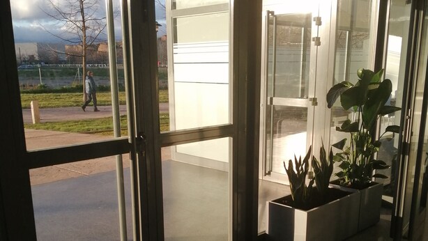 A hotel entrance with glass doors, a doormat, and a sign indicating an emergency exit. - Residencia La Ribera (Logroño)