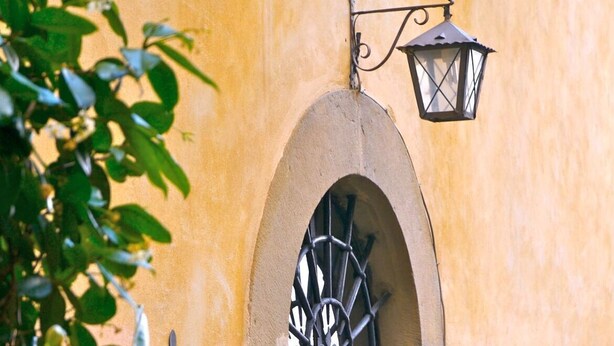 Una entrada de edificio con una reja de hierro forjado, un farol colgante y una cesta de flores.