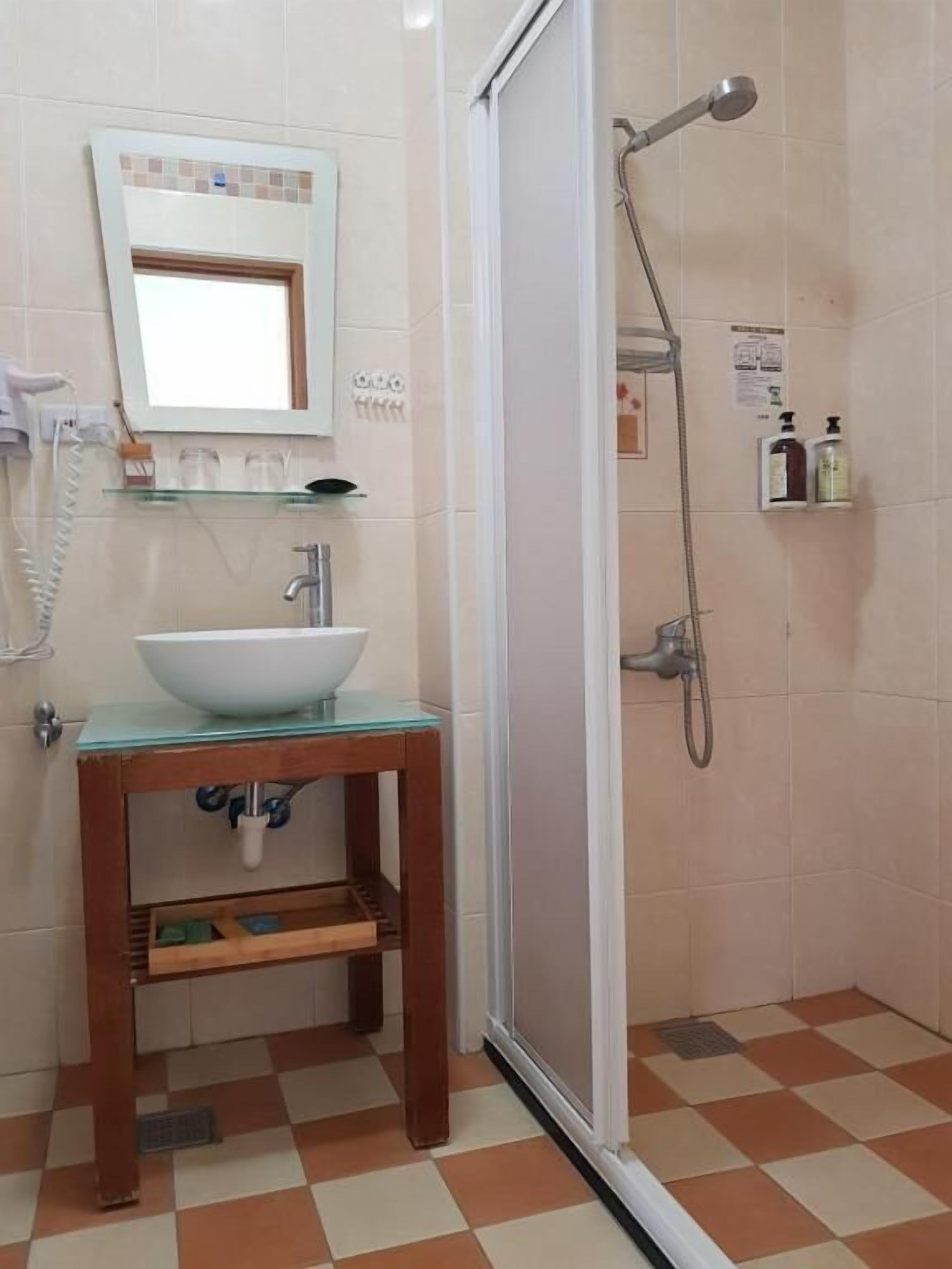 A bathroom with a glass sink, a mirror, a shower, and a tiled floor.