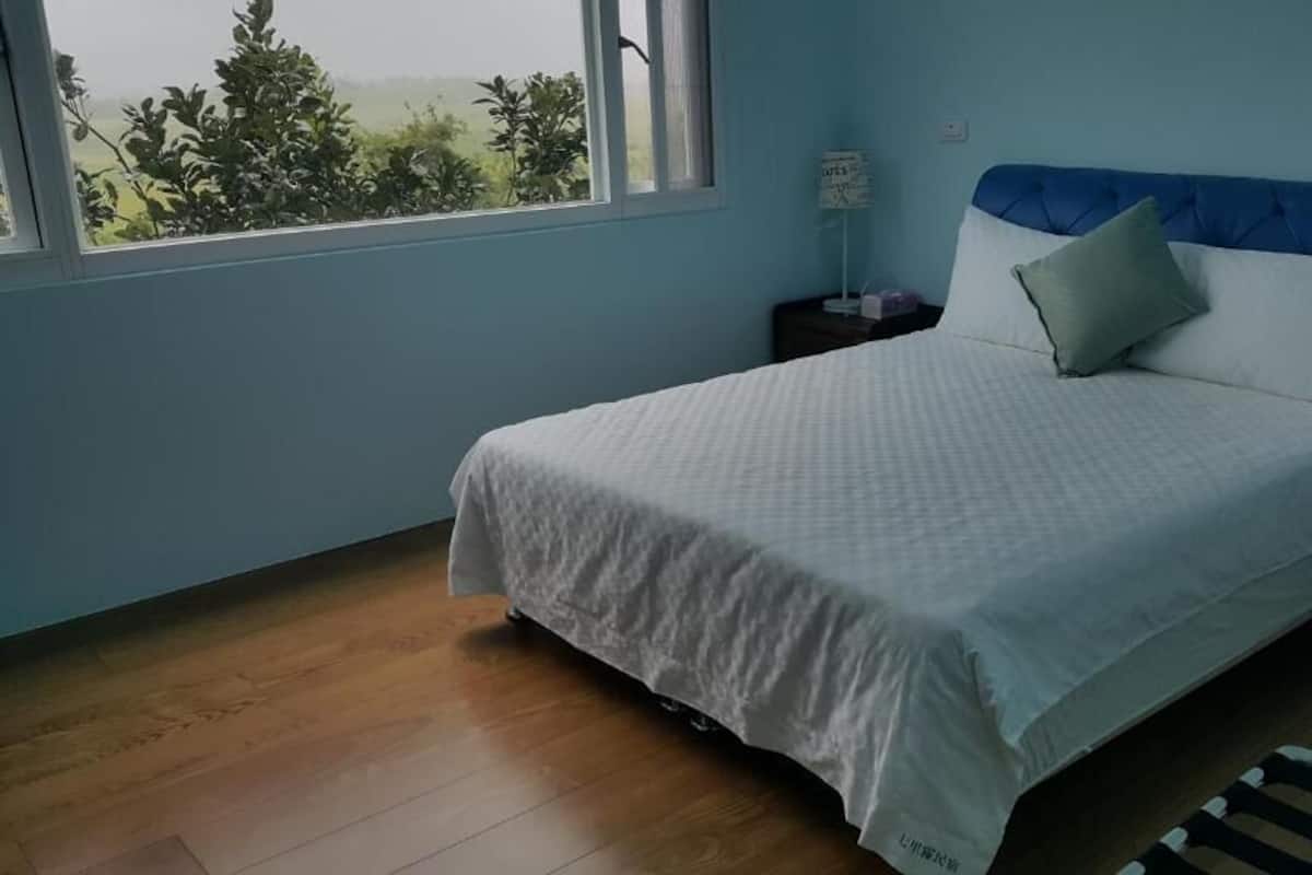 A bedroom with a bed, a nightstand, a window, and a view of greenery outside.