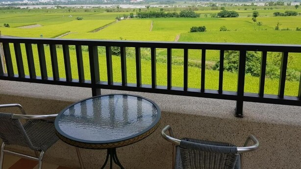 A balcony with a table and chairs, overlooking a green landscape with fields and mountains in the distance. - 7 Milefog B&B (Yuli)