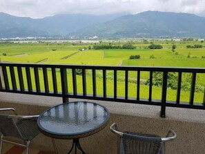 A balcony with a table and chairs, overlooking a green landscape with fields and mountains in the distance. - 7 Milefog B&B (Yuli)