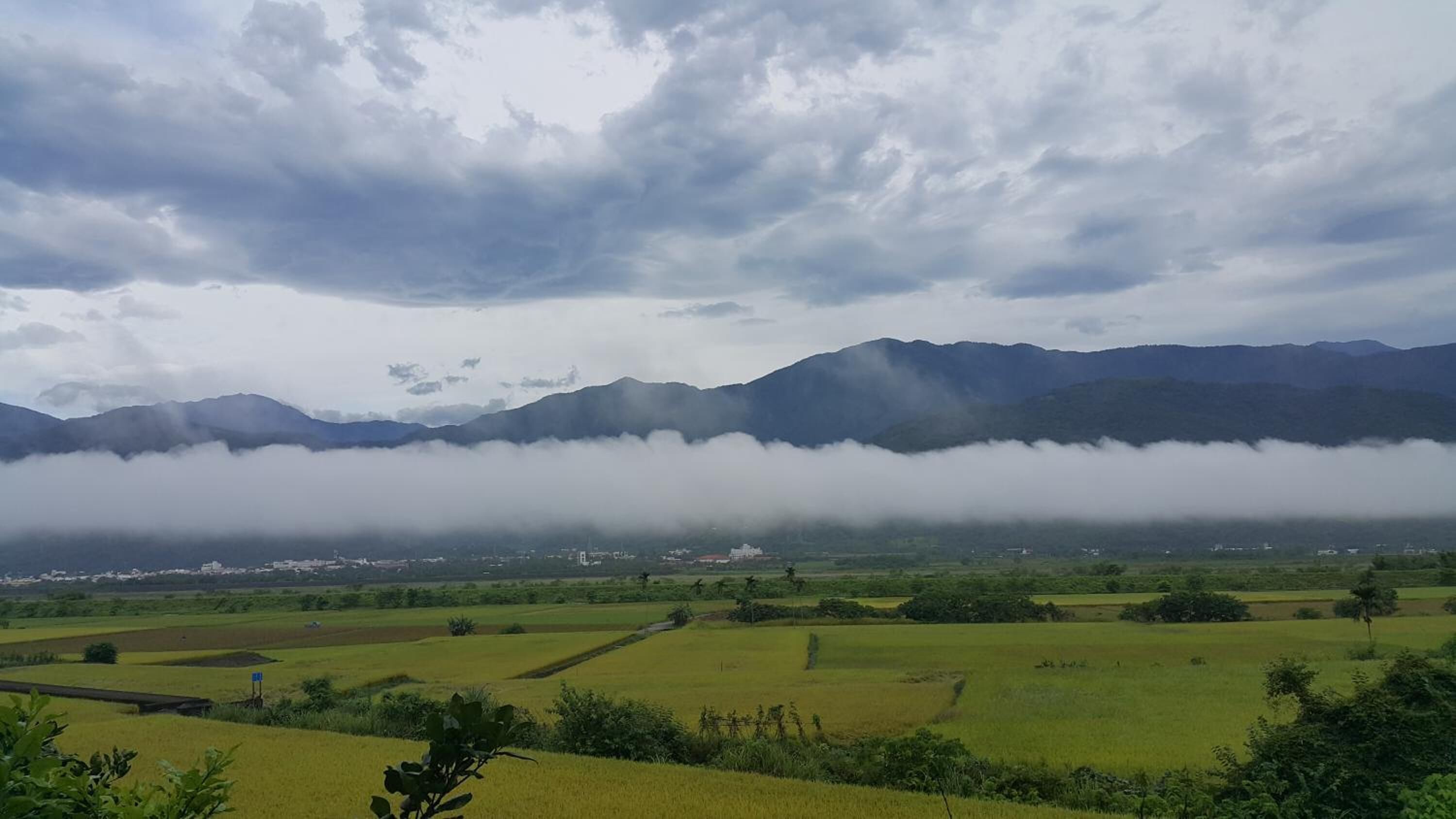 Un paisaje con campos verdes, una cordillera y un pueblo en el valle.