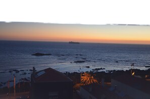 Une vue côtière avec un navire à l’horizon, une côte rocheuse et des bâtiments ornés de drapeaux.