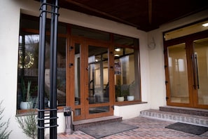 A hotel entrance with wooden doors, a black metal post, and a small trash bin. - Melania (Uman)