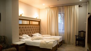 Un dormitorio con una cama grande, dos mesitas de noche, una silla y un ventanal con cortinas.