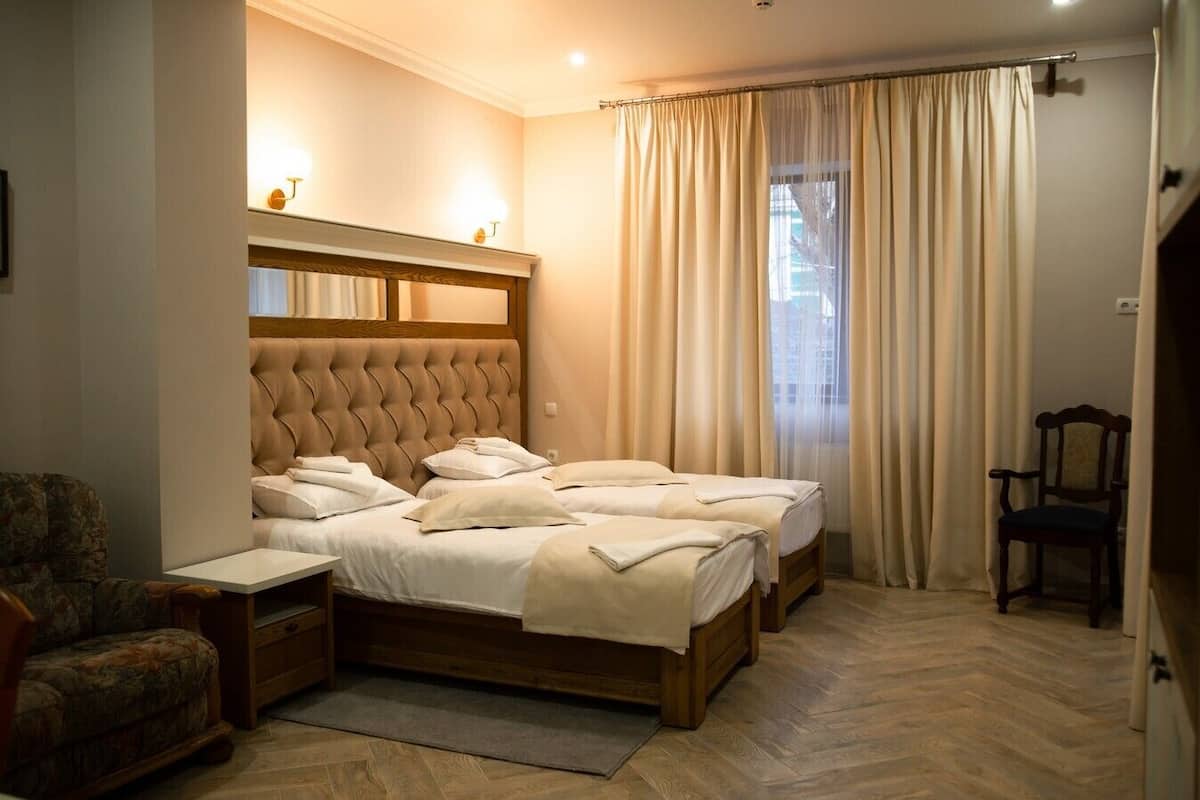 Un dormitorio con una cama grande, dos mesitas de noche, una silla y un ventanal con cortinas.
