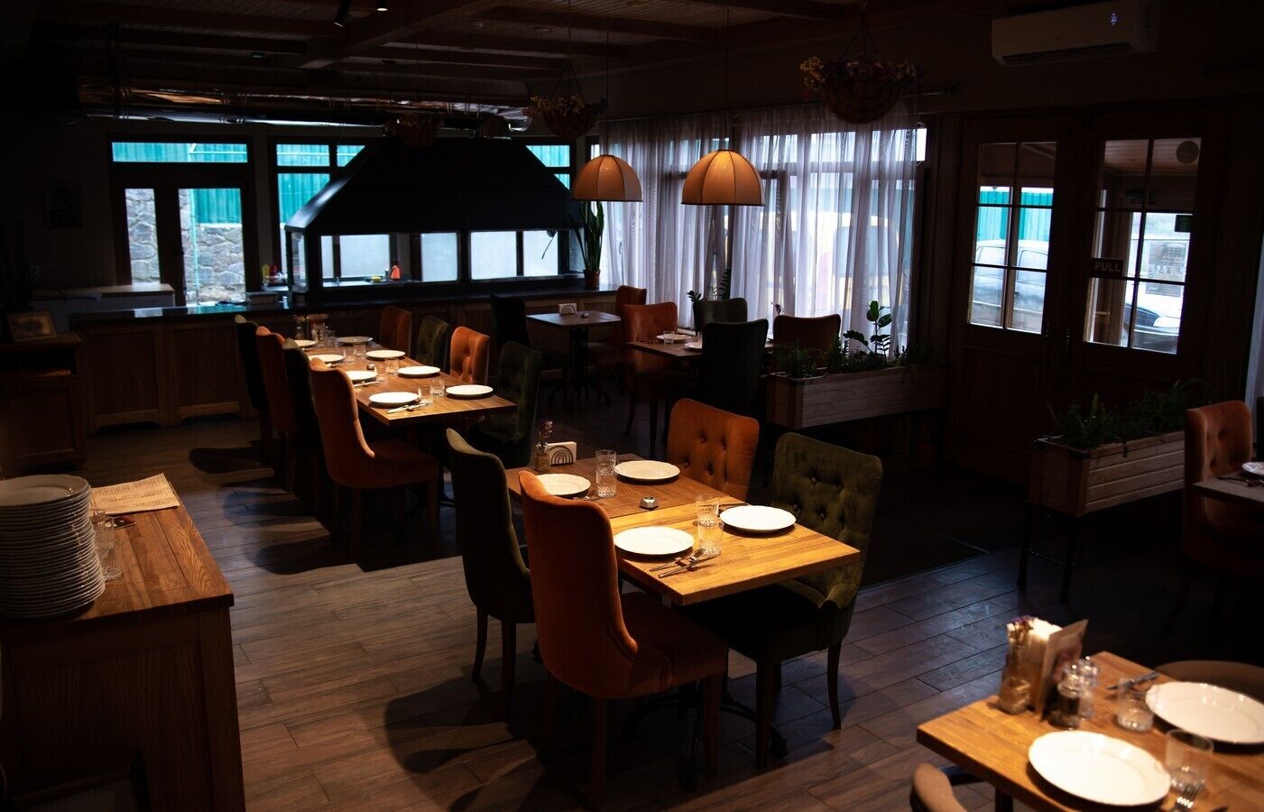 A restaurant with wooden tables and chairs, large windows, and hanging lamps.
