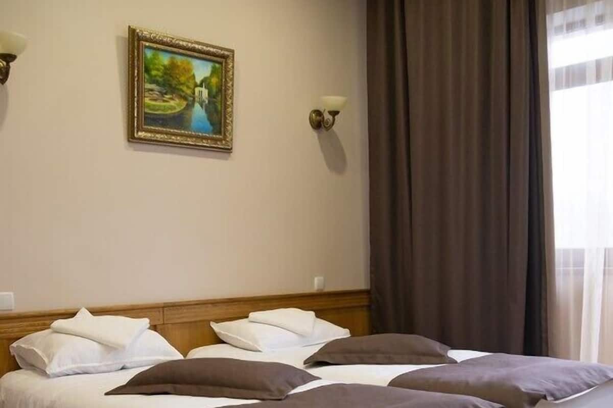 Una habitación con dos camas de madera, paredes color beige, un cuadro enmarcado y una ventana con cortinas.