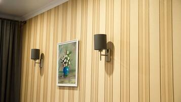 A wall with vertical stripes, a framed painting of a vase with flowers, and two wall-mounted light fixtures.