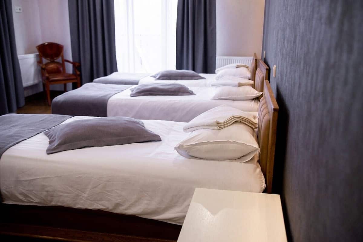 Habitación de hotel con dos camas, cada una con ropa blanca y almohadas, cabeceros de madera y una silla en la esquina.