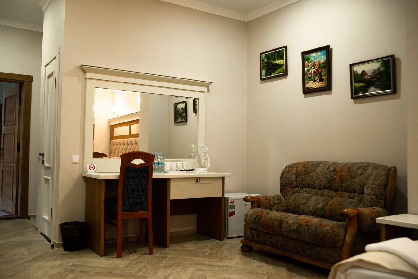 A room with a wooden desk, a chair, a large mirror, and a couch. There are three framed pictures on the wall.