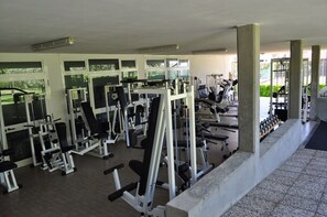 Un gimnasio con diferentes máquinas de ejercicio, amplias ventanas y un pilar de hormigón.