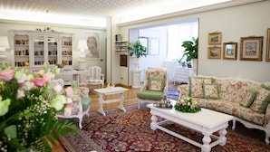 A living room with a floral sofa, a white coffee table, and a bookshelf. - Hotel Garden (Garda)