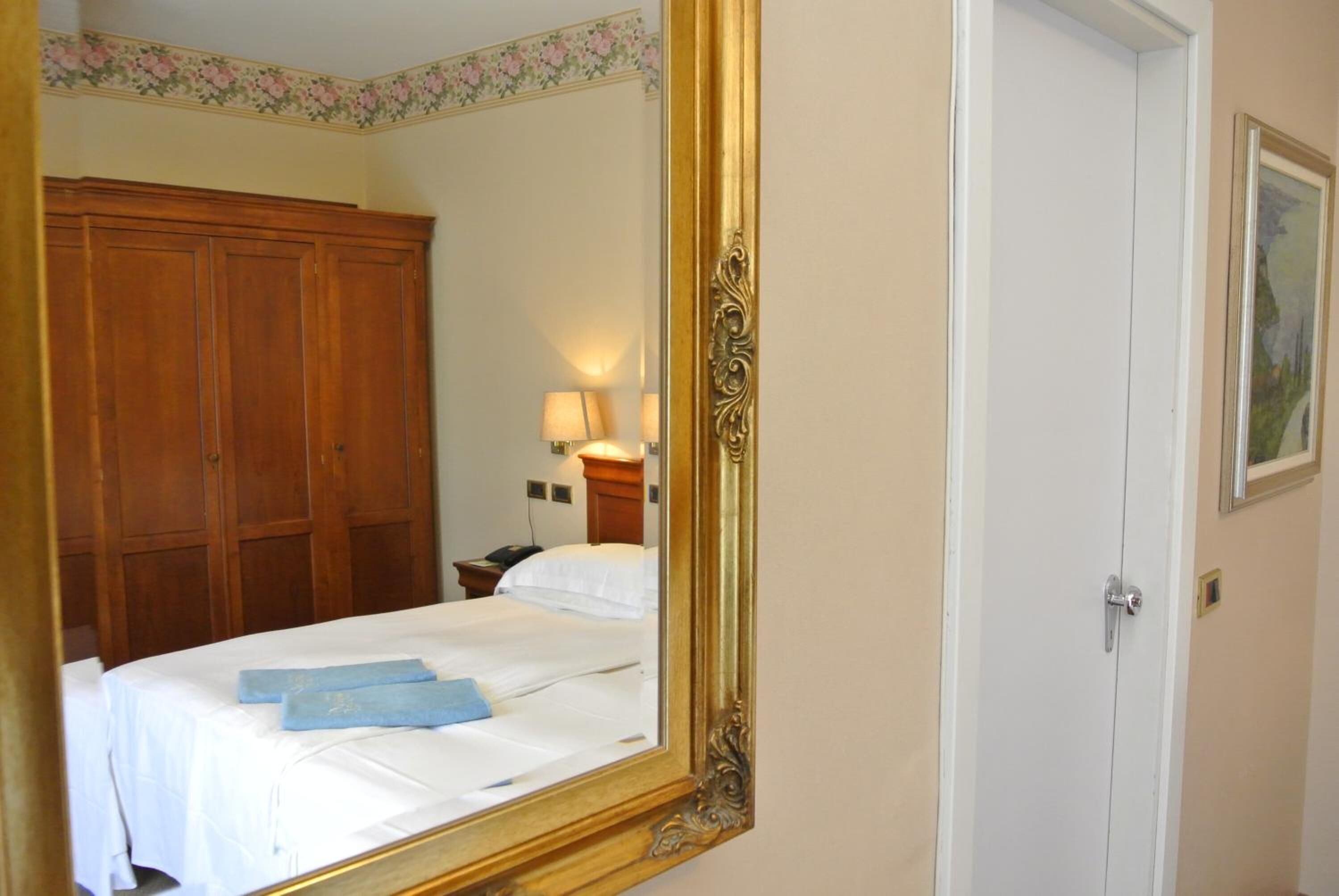 Una camera d'albergo con un letto grande, un armadio in legno, un comodino con una lampada e un quadro appeso al muro.