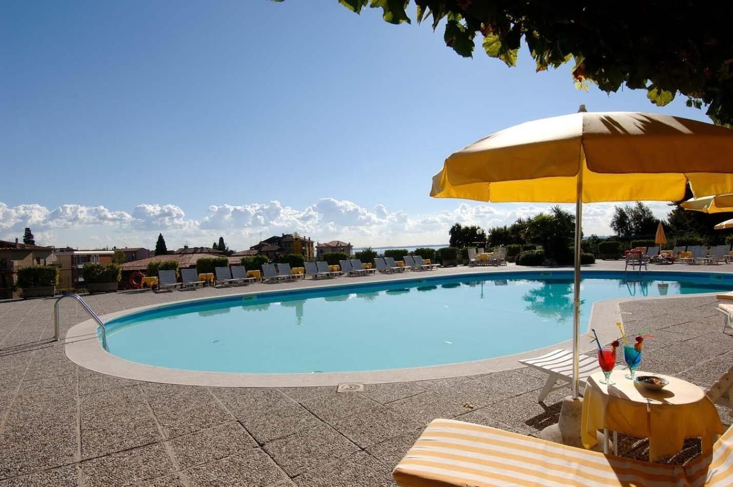 A swimming pool with lounge chairs and umbrellas, surrounded by buildings and trees.
