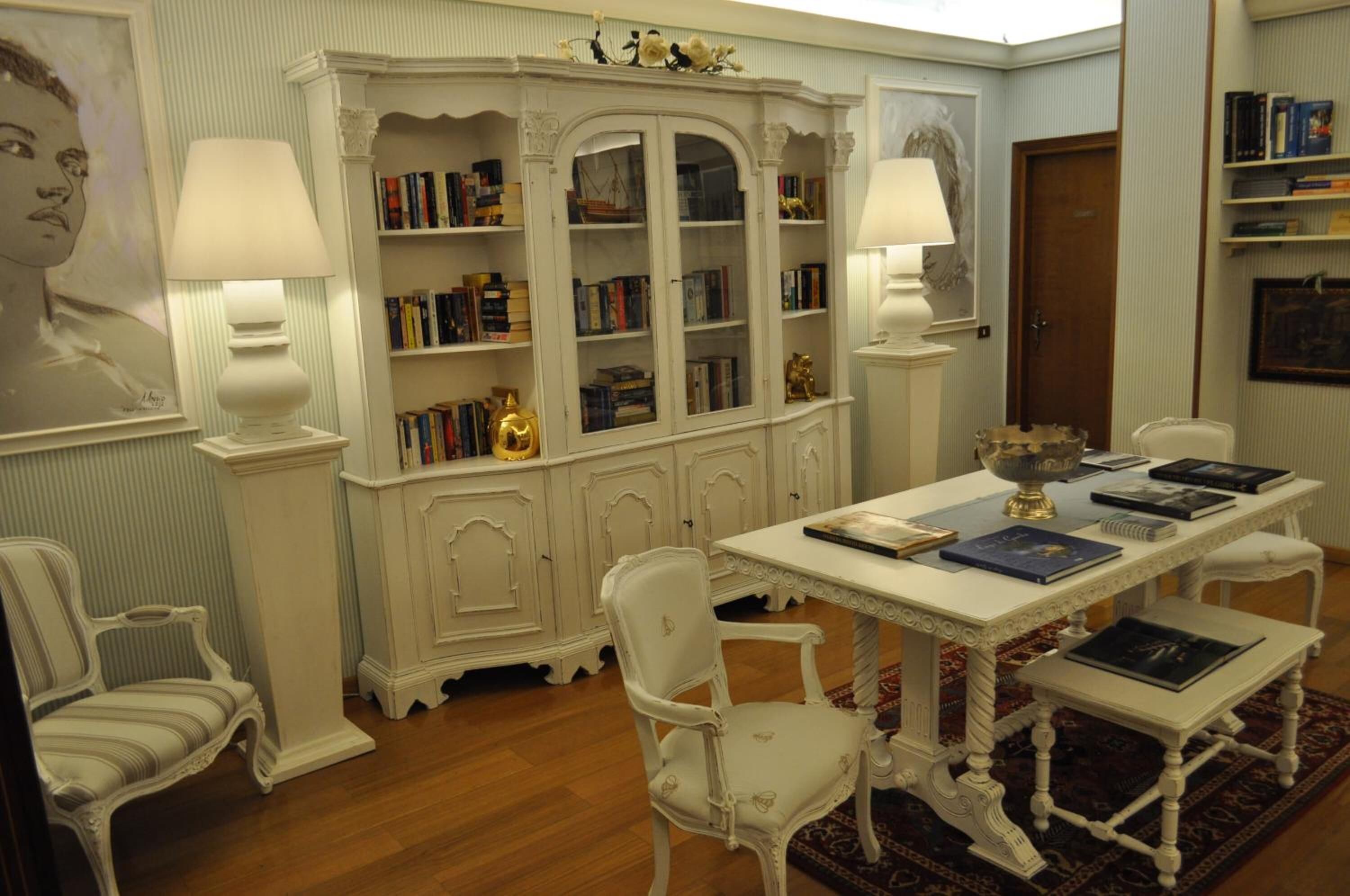 Zona de menjador amb taula blanca, cadires i una biblioteca plena de llibres.