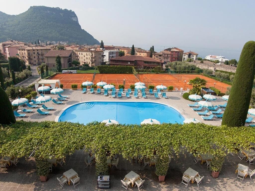 Area piscina con lettini e ombrelloni, circondata dal verde e con edifici sullo sfondo.