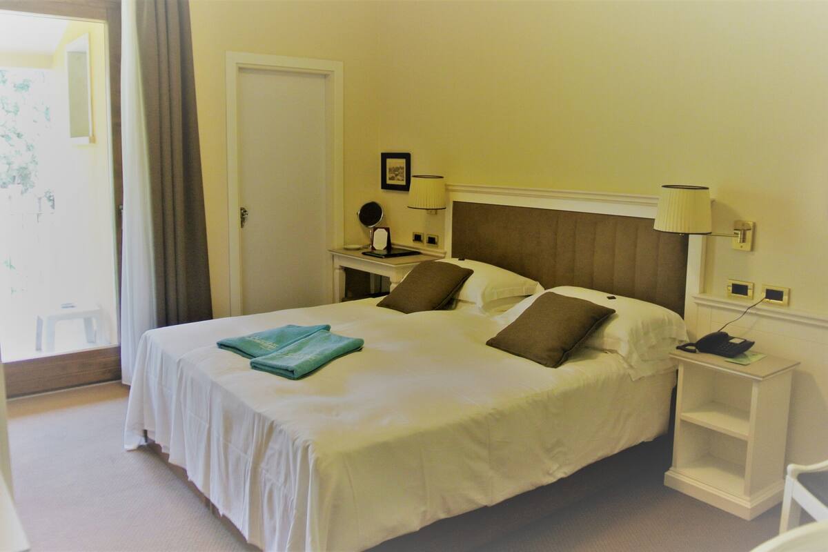 A hotel room with a bed, a nightstand, a lamp, a chair, and a door.