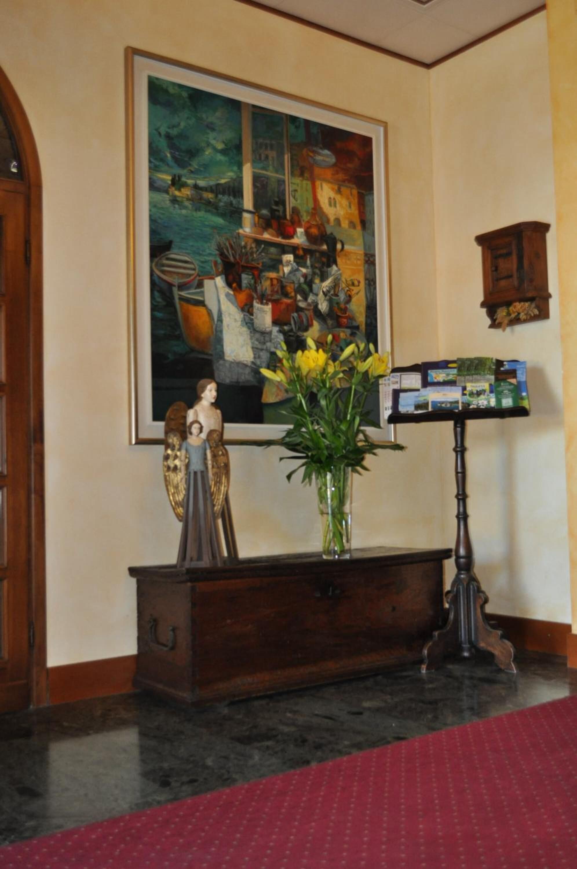 A room with a large painting, a wooden cabinet, a vase with flowers, and a small angel figurine.